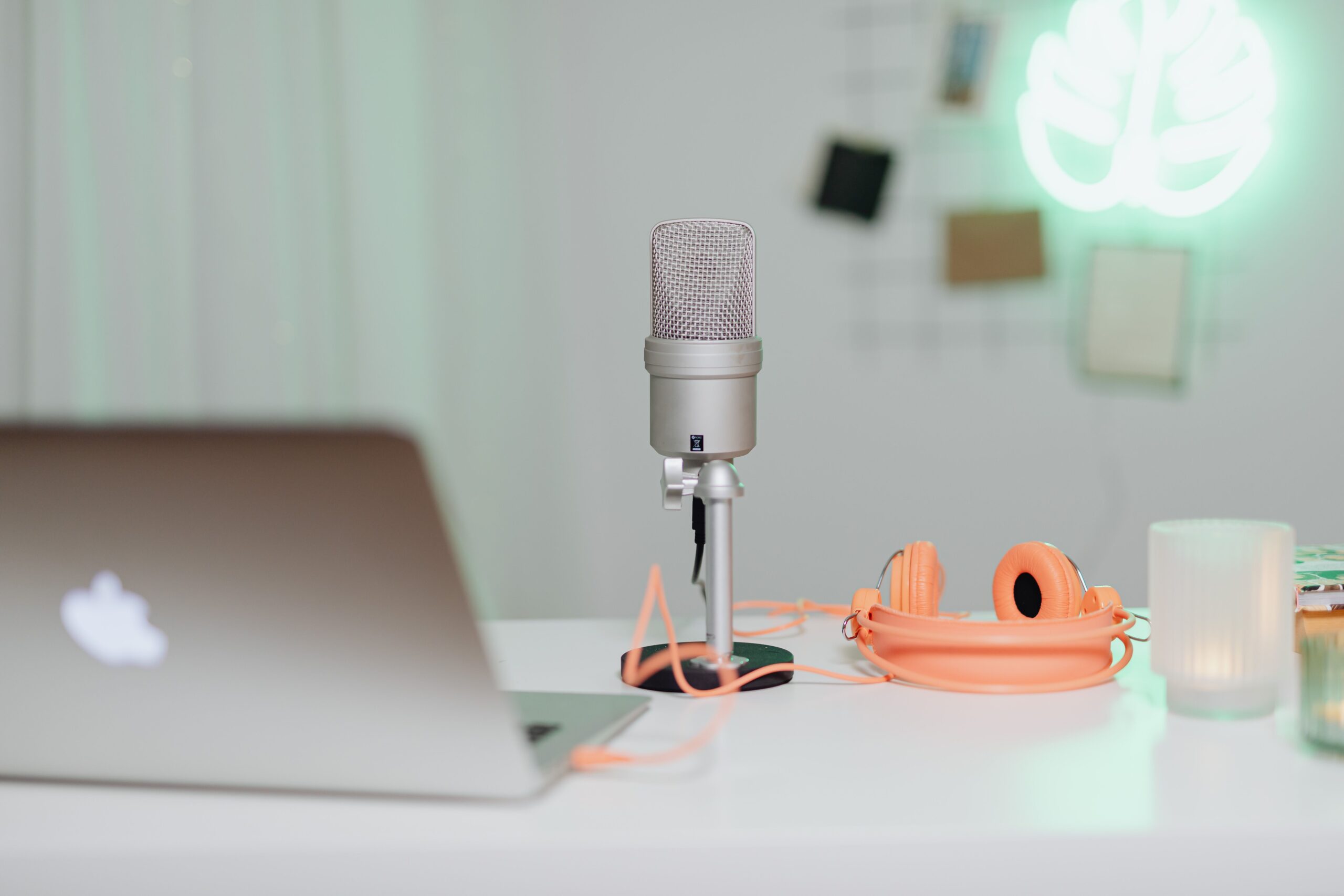 Silver condenser microphone on desk stand next to laptop and coral pink headphones